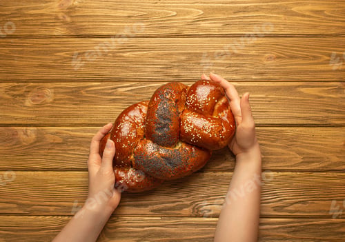 Preview: Female hands holding freshly baked Challah bread covered with poppy and sesame seeds, top view on