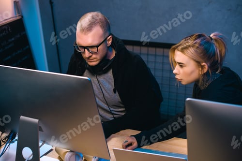 Preview: young couple of hackers looking at computer screen together at workplace