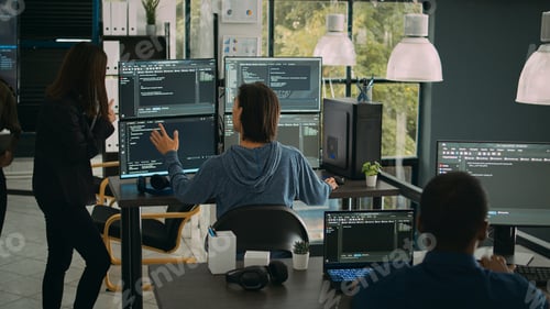 Preview: System engineer checking code on multiple monitors and working with app developer