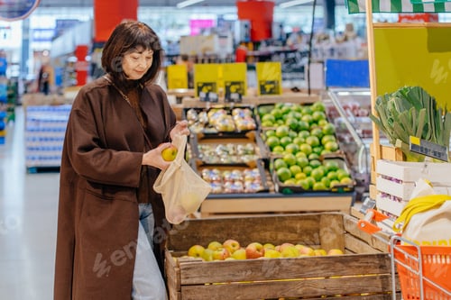 Preview: Brown haired female shopper in her 55s placing apples