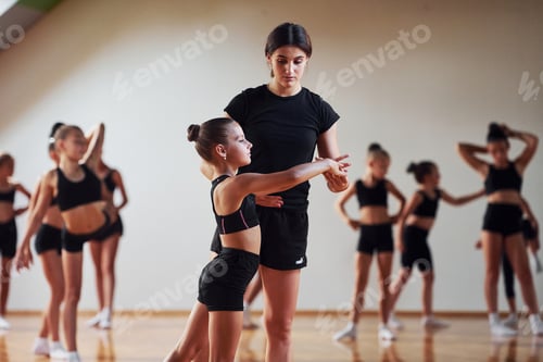 Preview: Woman teaching and helping. Group of female kids practicing athletic exercises together indoors