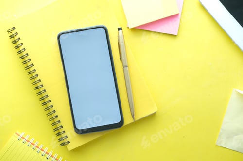 Preview: top view of smart phone and notepad on yellow background