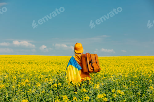 Preview: Woman in yellow hoodie with ukrainian flag and suitcase in rapeseed field
