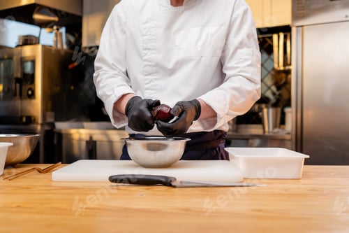 Preview: close up assistant chef in the kitchen in white jacket cuts beets in his hands over the table