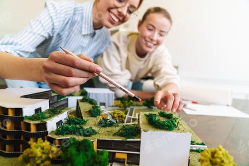 Preview: Photo of joyful young women architect designing draft with house model
