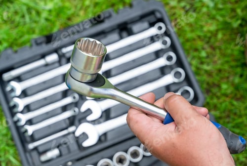Preview: Man's hand holds a metal tool over a box with a set of tools supplies for construction work closeup