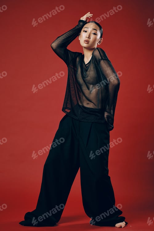 Preview: Fashionable asian woman in black outfit striking a pose on red background with hands on hips and