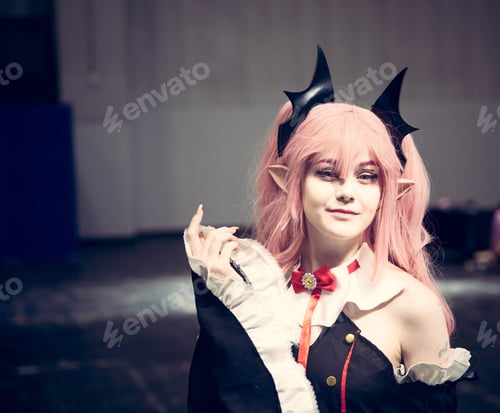 Preview: A pretty cosplay girl as Japanese Anime character with pink hair and bat ears at at comic con event