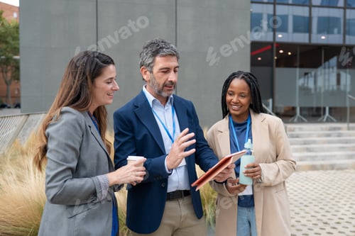 Preview: Diverse business team discussing project using digital tablet outdoors