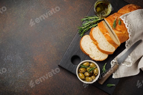 Preview: Italian traditional Ciabatta bread with olives, olive oil, pepper and rosemary on a dark stone or co