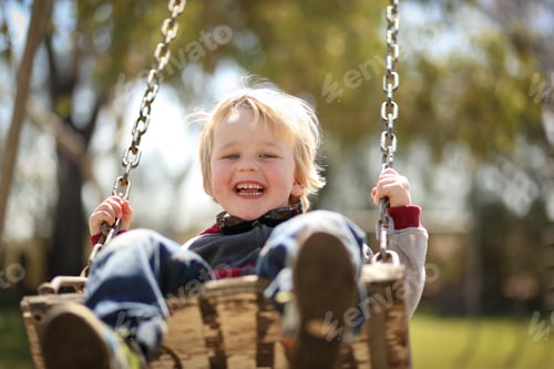 Preview: Happy adorable blonde Australian kid swinging in the playground