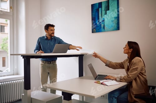 Preview: Happy entrepreneur passing documents to his colleague while working in the office