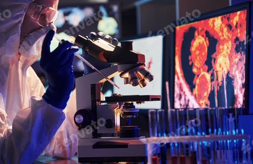 Preview: Scientist in white protective uniform near displays with data works with coronavirus and blood tubes