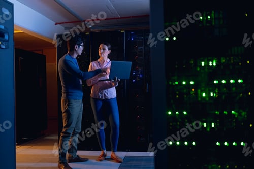Preview: Diverse male and female engineers using laptop in computer server room
