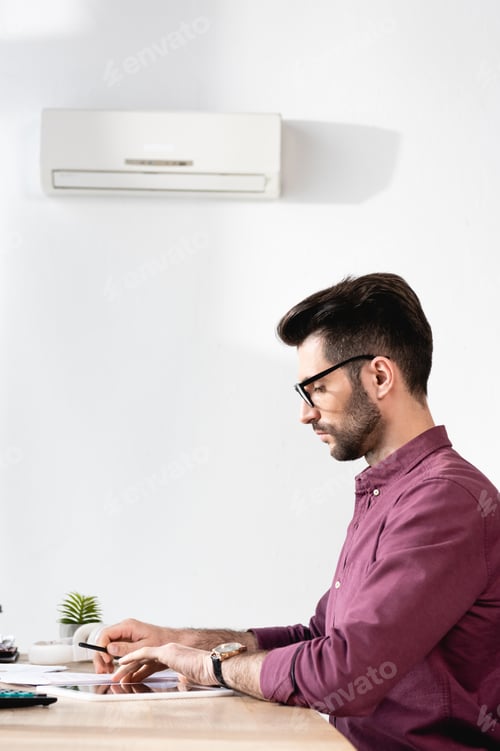 Preview: side view of handsome businessman sitting at workplace under air conditioner