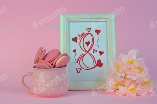 Preview: Beautiful shot of flowers with macaroons in a mug near a photo frame showing an eight of March