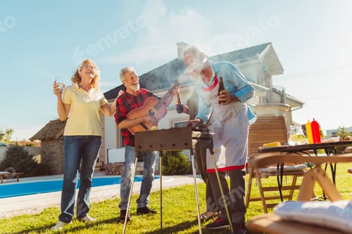 Preview: Senior friends having fun while making barbecue in the backyard