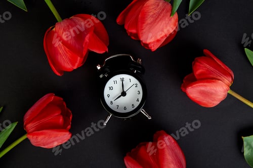 Preview: Black alarm clock near bouquet red tulips