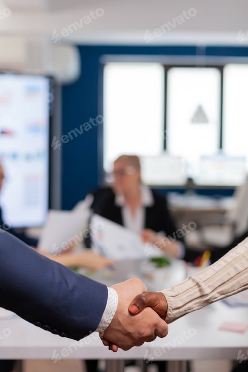 Preview: Close up of multiracial business partners standing in front of conference desk shaking hands