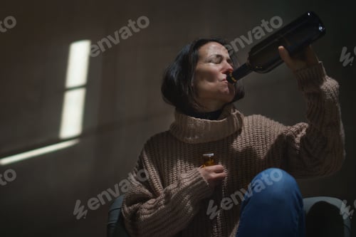 Preview: Depressed drunk woman sitting on the floor in the dark taking pills and drinking wine from a bottle