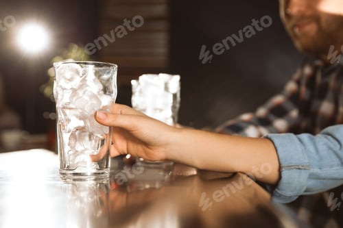 Preview: Woman holding glass with ice cubes for cola at bar counter