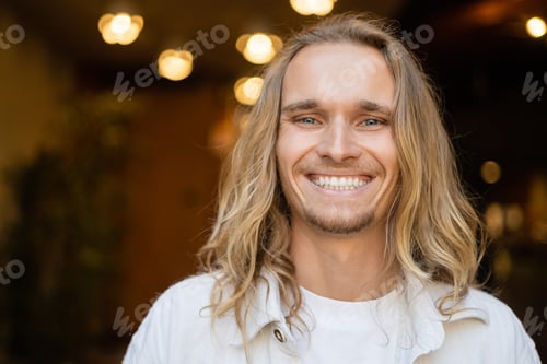 Preview: portrait of overjoyed long haired yoga man smiling at camera near blurred lights outdoors
