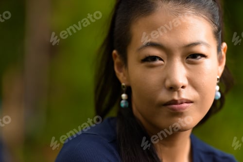Preview: Close-up portrait of beautiful rebel Asian woman face looking at camera outdoors