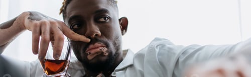 Preview: African american man with vitiligo in white shirt holding glass of whiskey at home, banner