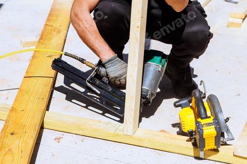 Preview: Construction worker uses nail gun to secure wooden frame during building works at construction site
