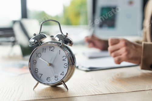 Preview: selective focus of vintage alarm clock near cropped businessman working on blurred background,