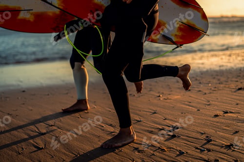 Preview: Two surfers with surfboard prepares to hit the waves at sunset.