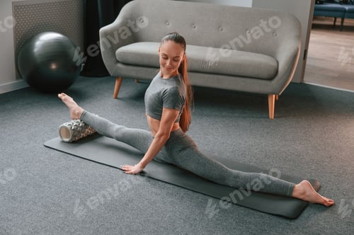 Preview: Big stretch for legs. Young woman in yoga clothes doing fitness indoors