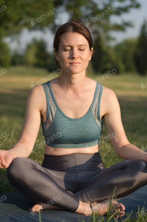 Preview: Beautiful young woman meditates in the park at sunset. Woman practices yoga in the park.