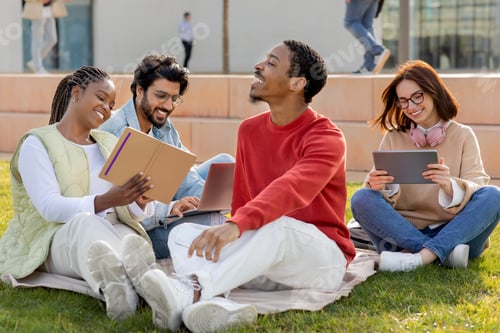 Preview: Cheerful international millennial students study, relax, sit on grass, watch online lesson on tablet