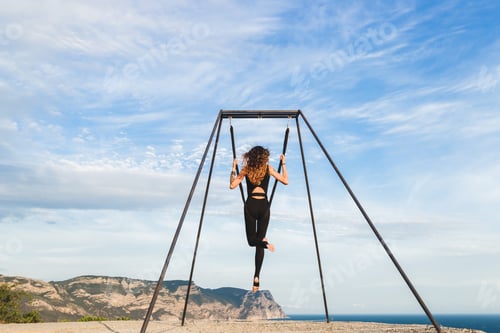 Preview: Woman practicing fly-dance yoga poses in a hammock on the coast with views of the mountains
