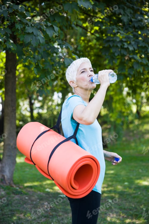 Preview: Senior woman holds fitness mat on her back in the park