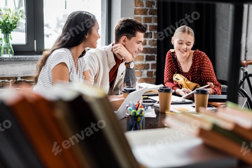 Preview: multiethnic students smiling and looking at digital tablet in apartment