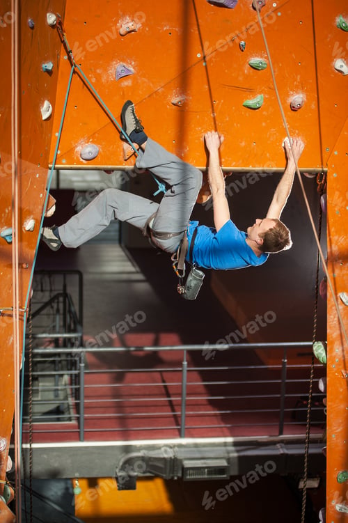 Preview: Male rock-climber practicing climbing on rock wall indoors