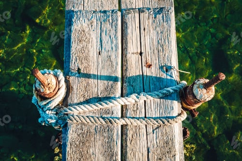 Preview: Closeup shot of a narrow wooden dock with two poles wrapped in rope in the sea