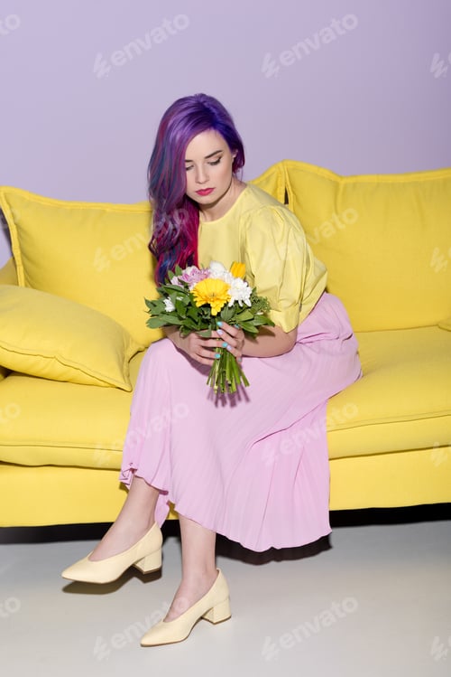 Preview: attractive young woman sitting on yellow couch with floral bouquet