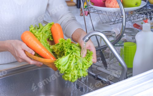 Preview: Woman hand is washing organic lettuce and carrot vegetables in the kitchen
