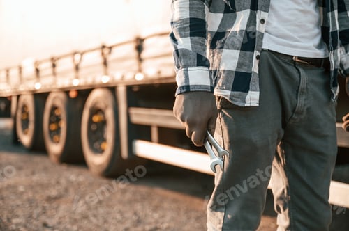 Preview: Close up view. Holding wrenches. Young truck driver is with his vehicle at daytime