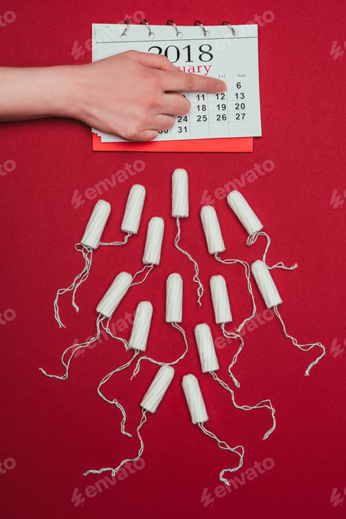 Preview: cropped shot of woman pointing at date in calendar with menstrual tampons around isolated on red