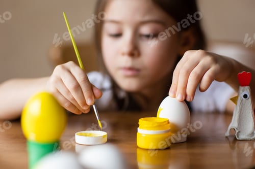 Preview: child paints eggs for Easter at home at table. kids craft - egg stand made from packaging carton