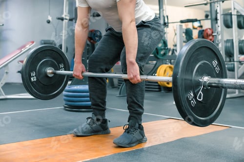 Preview: Closeup of arms and legs of man exercising with barbell at sport gym. Athlete, bodybuilding