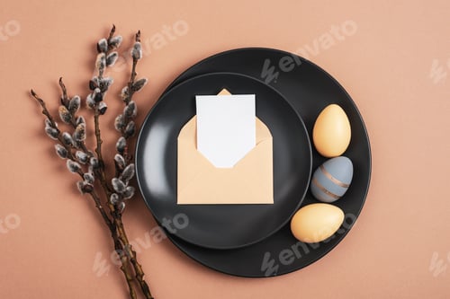 Preview: Black plates with painted Easter eggs, envelope with blank card and willow branches on beige