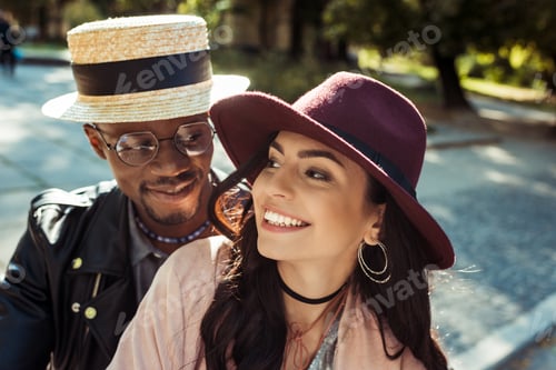 Preview: Lovely multicultural couple in hats walking in a park