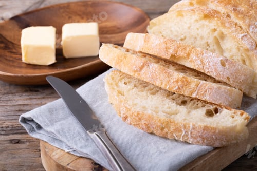 Preview: Sliced bread loaf on napkin by butter cubes in plate