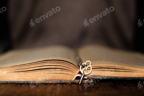 Preview: Open old book on wooden table with vintage key. Love for learning.