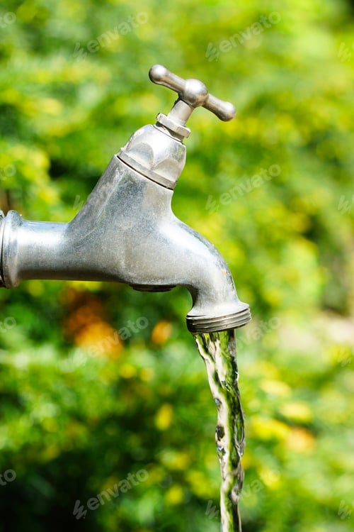 Preview: Vertical shot of water coming out of a faucet behind trees